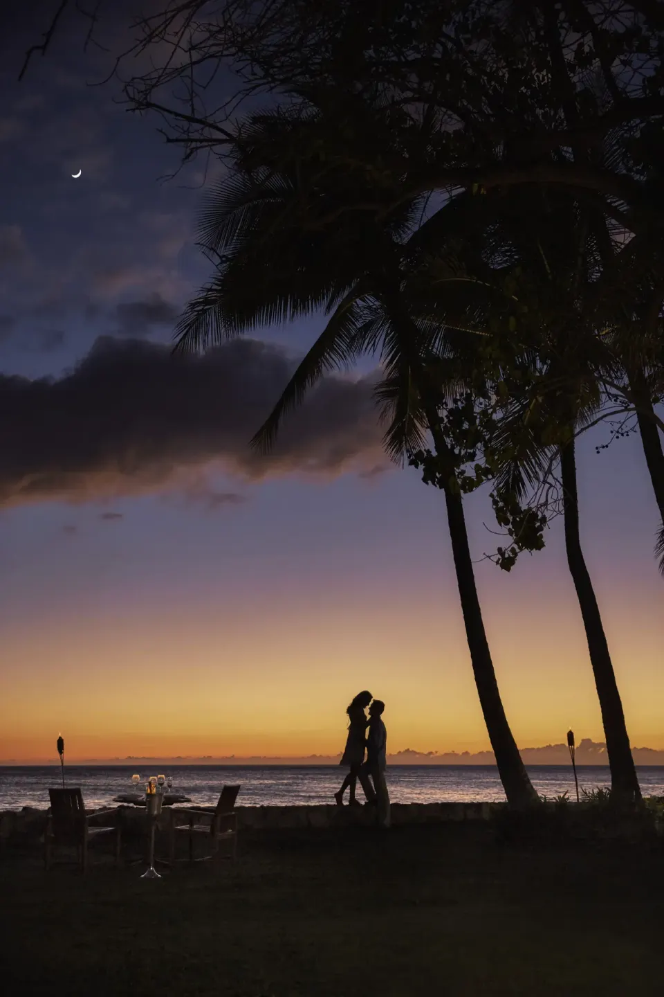 Couple walking beneath palm trees at sunset at Four Seasons Resort Oahu at Ko Olina.