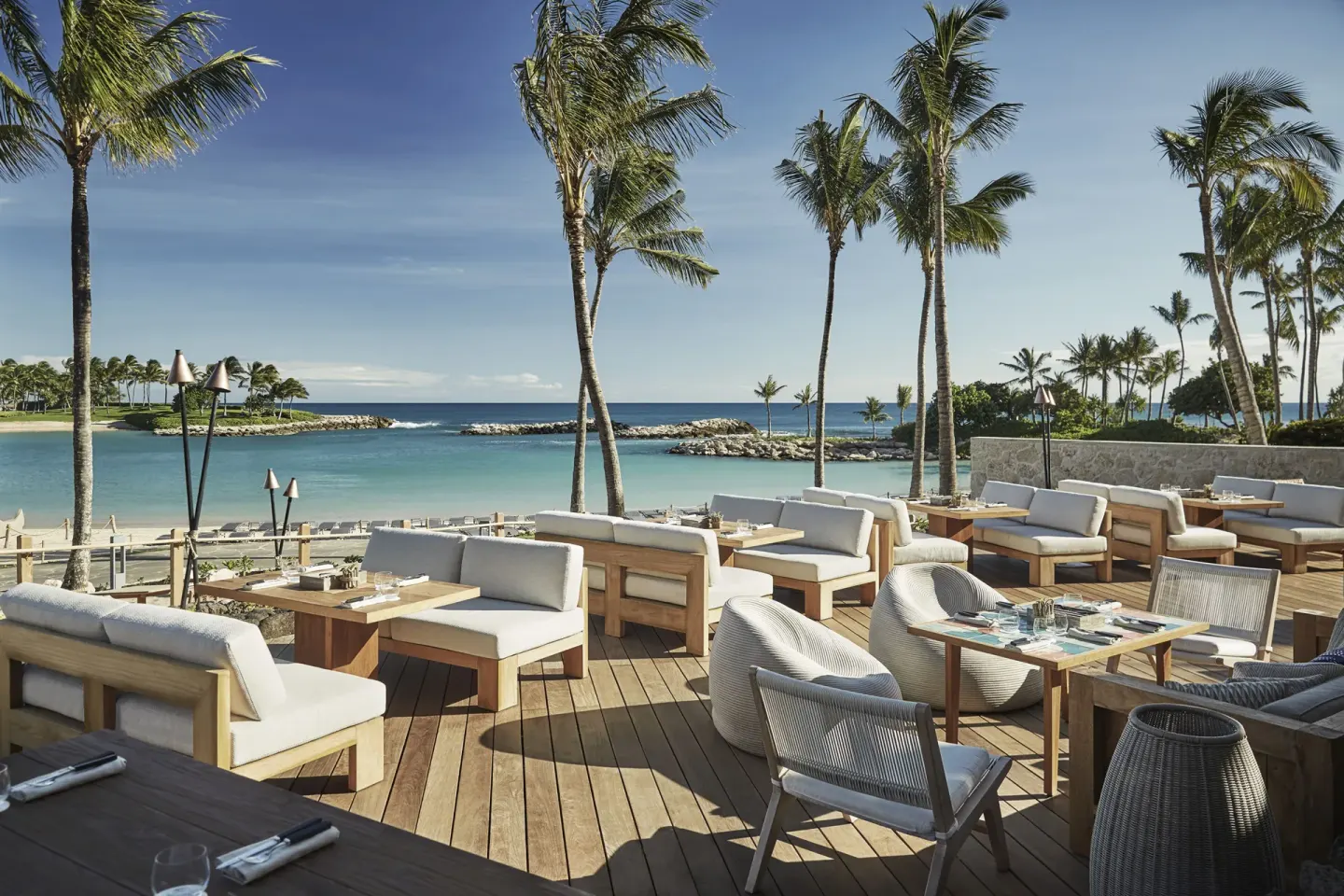 Oceanfront terrace seating with palm trees at Four Seasons Resort Oahu at Ko Olina.