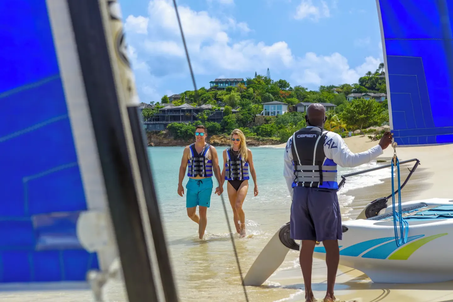 Guests in life vests walk from the surf to a catamaran at Galley Bay Resort & Spa.