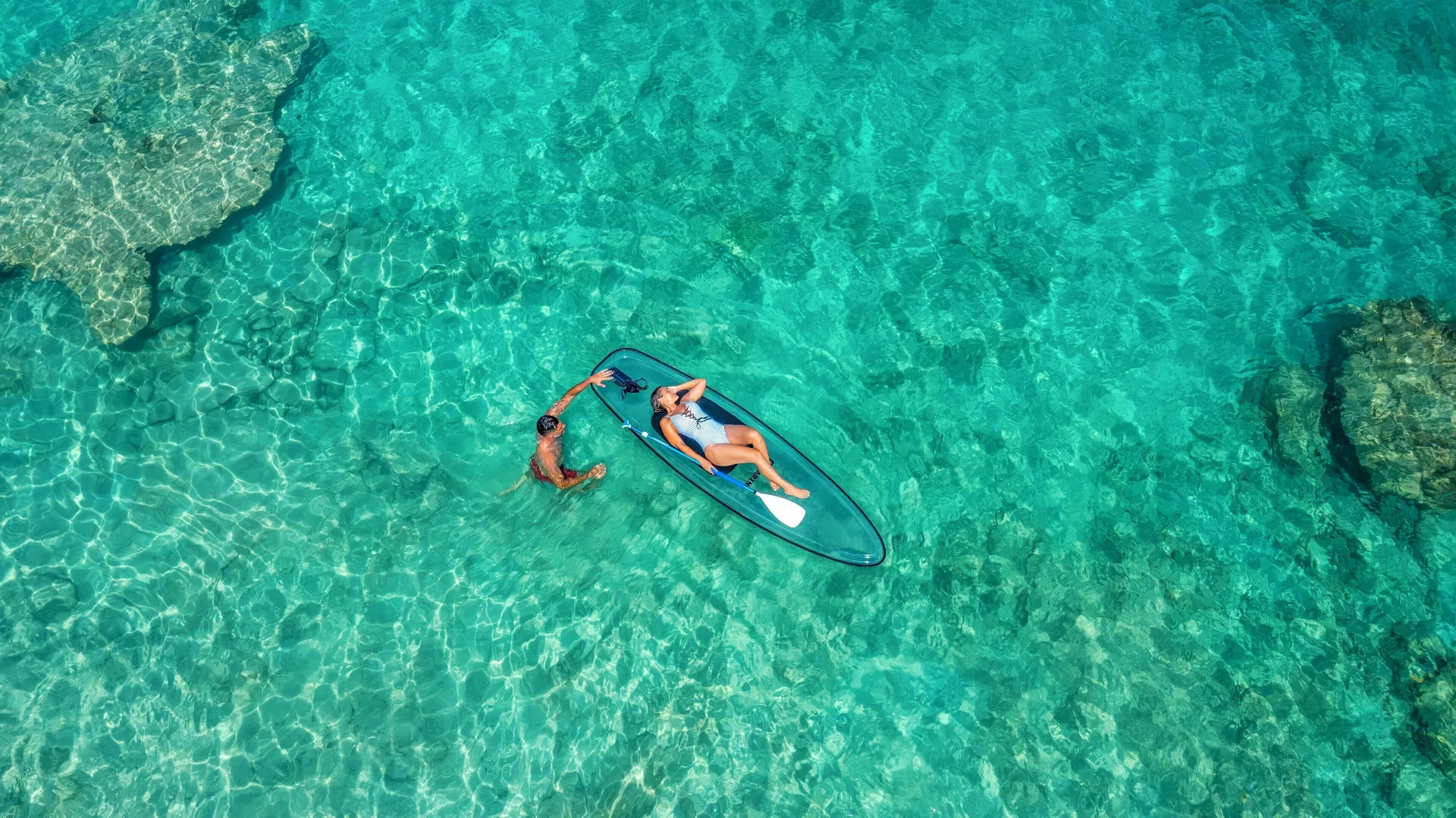 A swimmer and paddleboarder float over clear turquoise water at Galley Bay Resort & Spa.