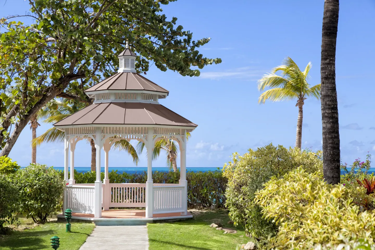White garden gazebo with ocean beyond the hedges at Galley Bay Resort & Spa.