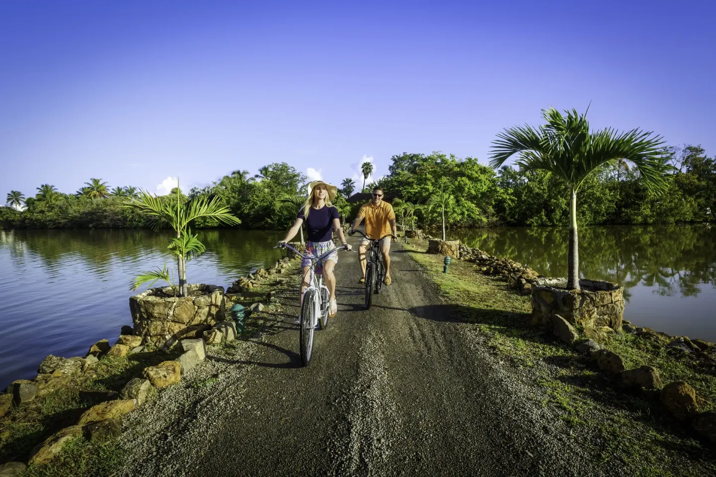 Two guests riding bicycles on a lagoon path at Galley Bay Resort & Spa.