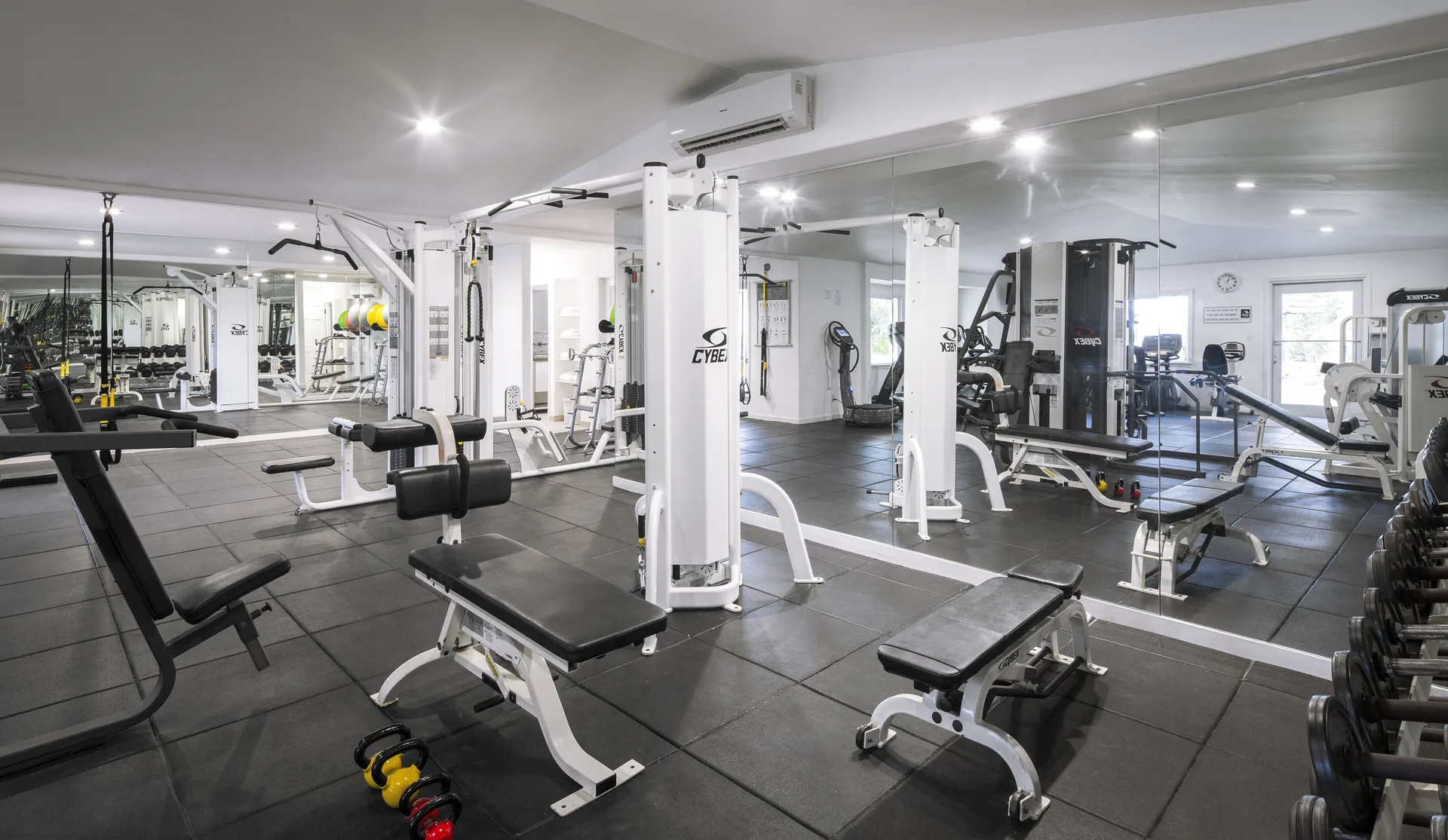 Mirrored fitness center with benches, cable machines, dumbbells, and kettlebells at Galley Bay Resort & Spa.