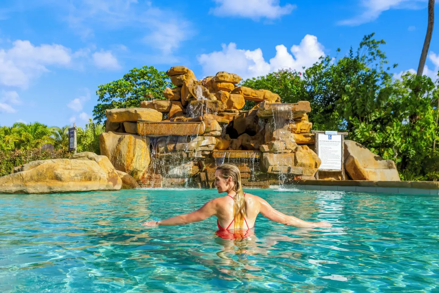 Guest swimming in the pool facing a rock waterfall at Galley Bay Resort & Spa.