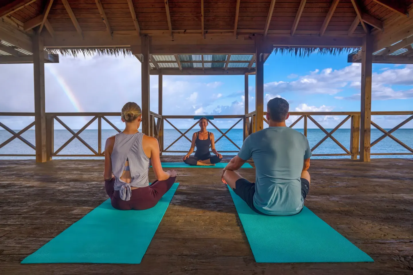 Yoga class seated on mats in an oceanfront pavilion with a rainbow at Galley Bay Resort & Spa.