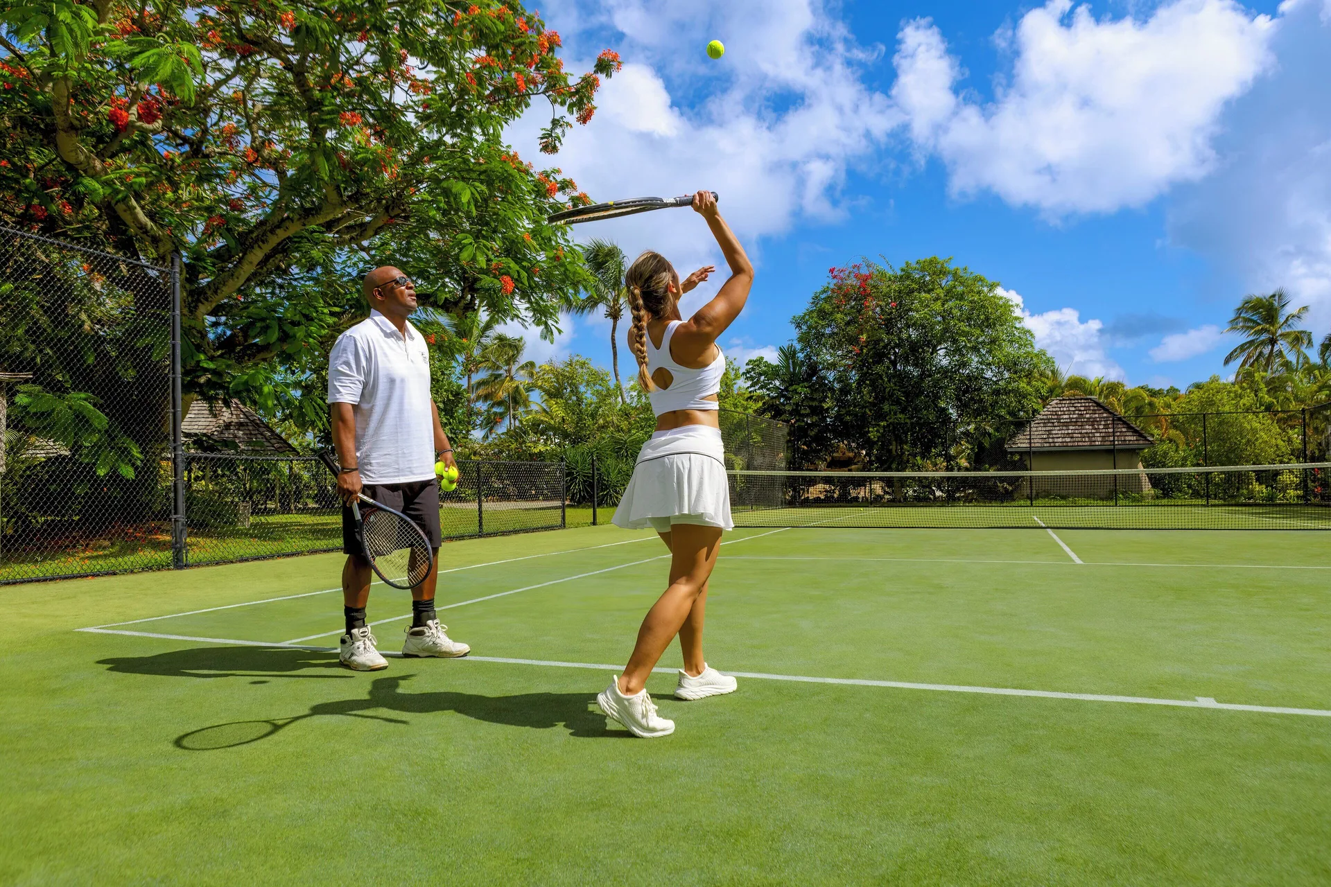 Two guests practice tennis on a sunny court at Galley Bay Resort & Spa.
