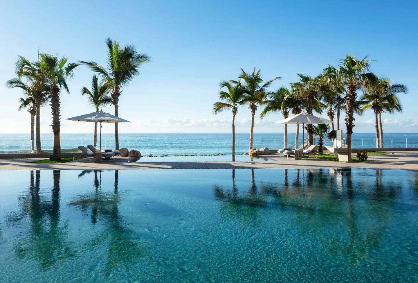 Calm pool reflecting palms by the ocean at Garza Blanca Los Cabos.