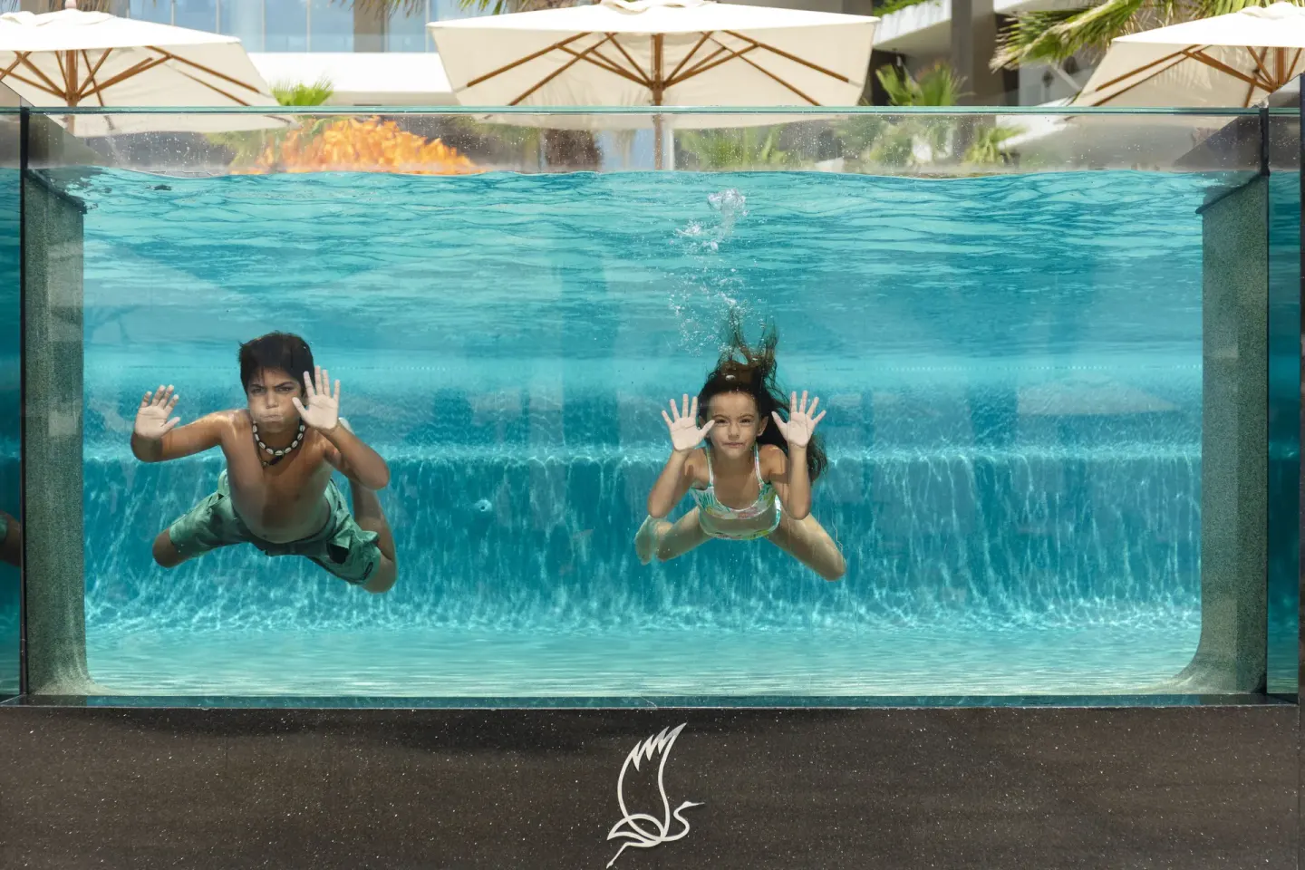 Two children swimming behind a clear pool wall at Garza Blanca Los Cabos.