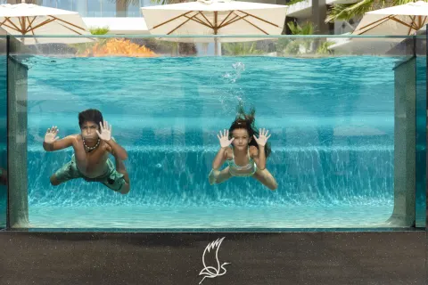 Two children swimming behind a clear pool wall at Garza Blanca Los Cabos.