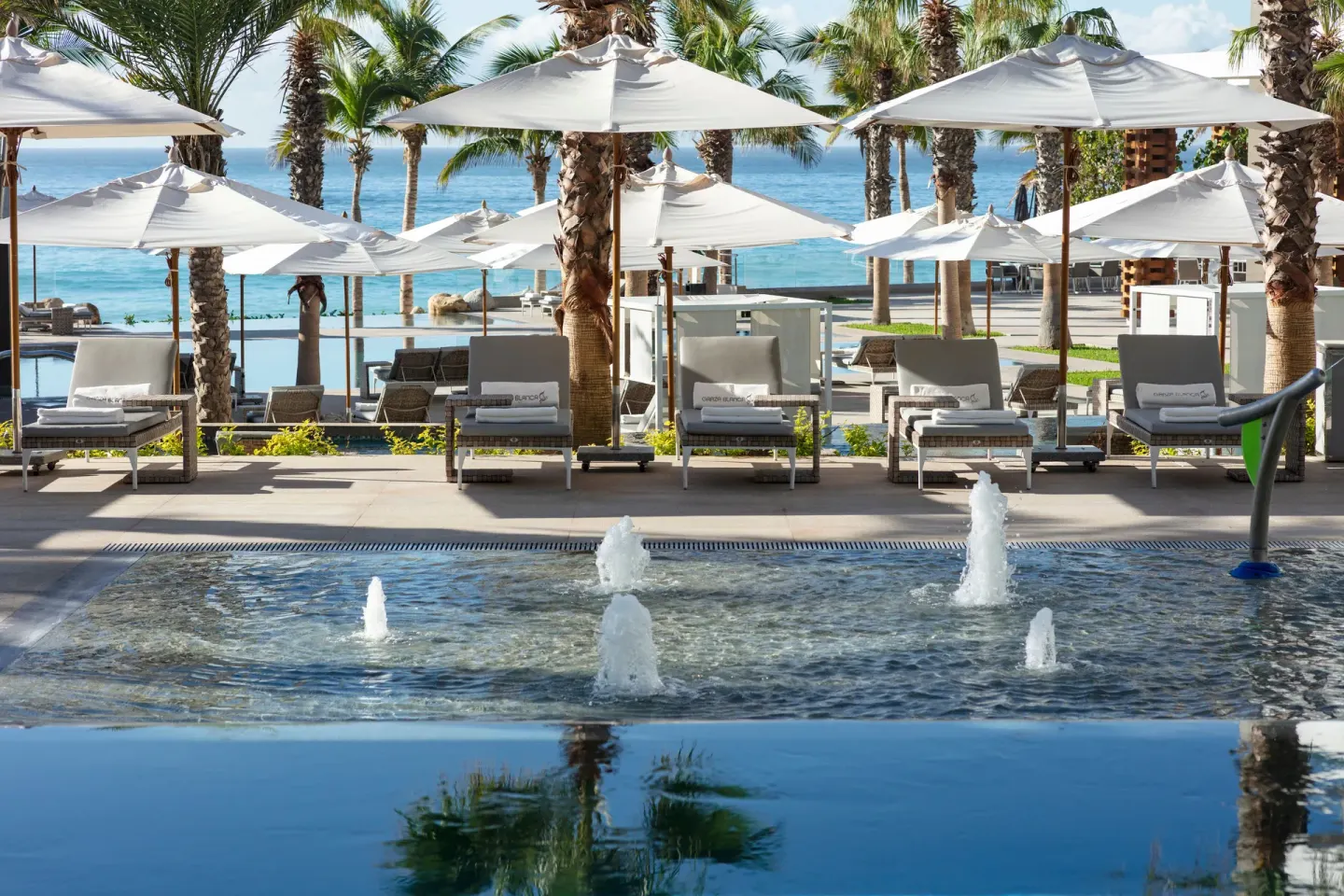 Fountain pool, loungers, white umbrellas, palms, and ocean at Garza Blanca Los Cabos.