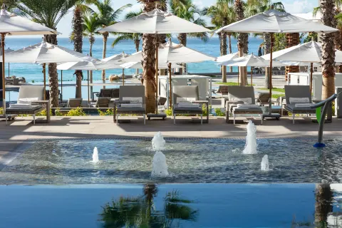 Fountain pool, loungers, white umbrellas, palms, and ocean at Garza Blanca Los Cabos.