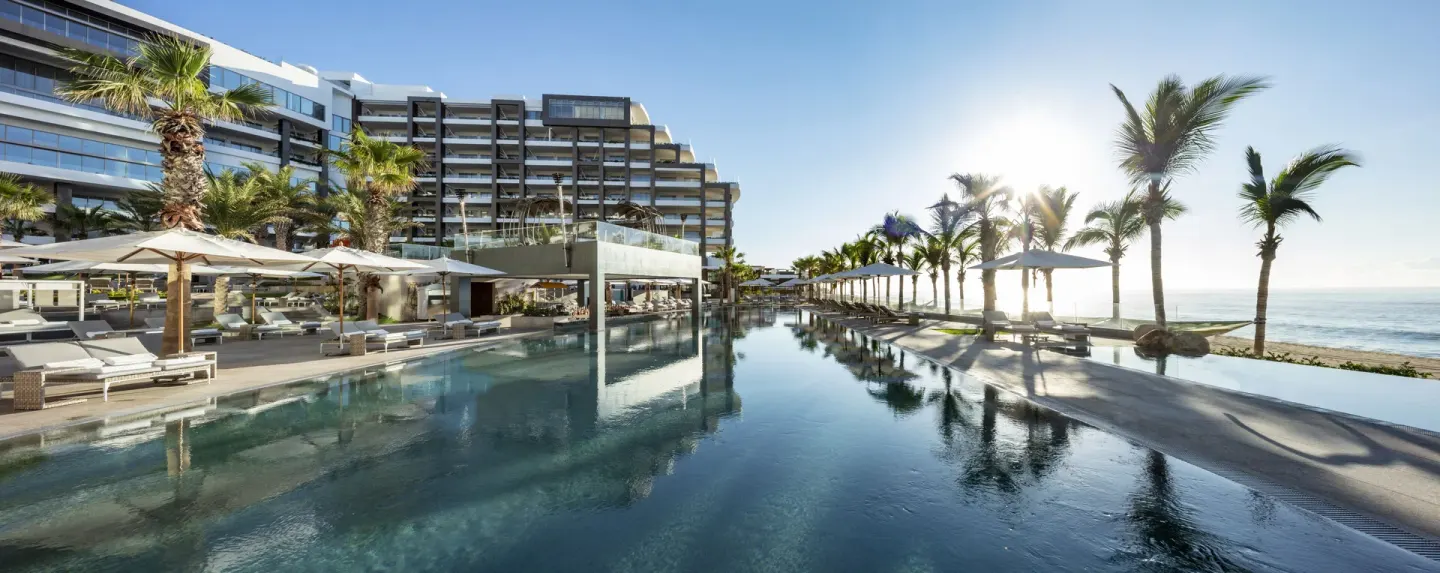 Long oceanfront pool with palms, umbrellas, loungers, and resort building at Garza Blanca Los Cabos.
