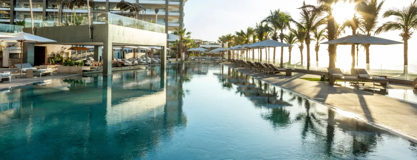 Main pool with palm trees, loungers, and sunset light at Garza Blanca Los Cabos.
