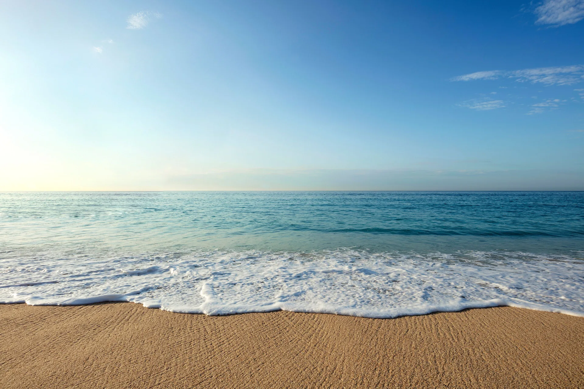 Ocean waves washing onto sandy beach under a clear sky at Garza Blanca Los Cabos.