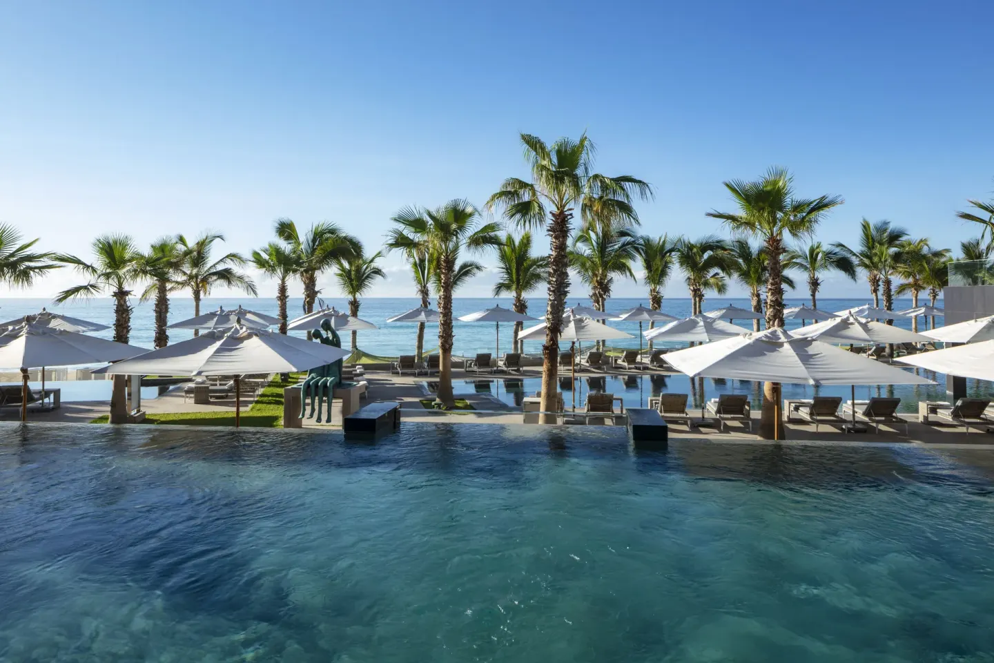 Oceanfront pool with palms, loungers, and white umbrellas at Garza Blanca Los Cabos.