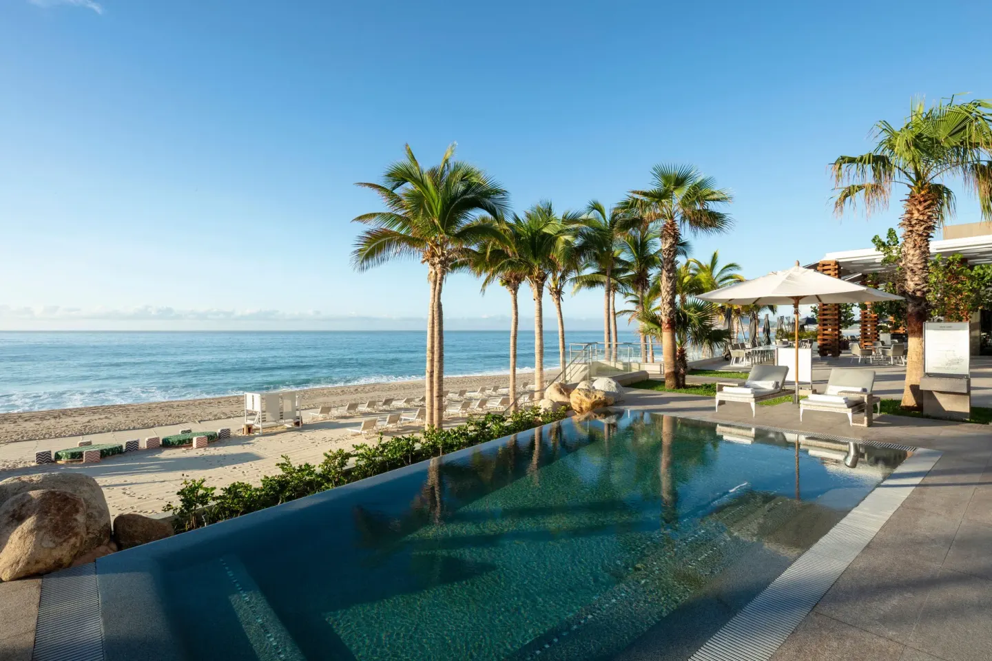 Oceanfront pool with palm trees and loungers at Garza Blanca Los Cabos.