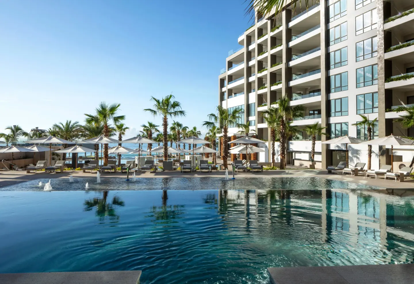 Pool deck with umbrellas, palms, and resort tower at Garza Blanca Los Cabos.