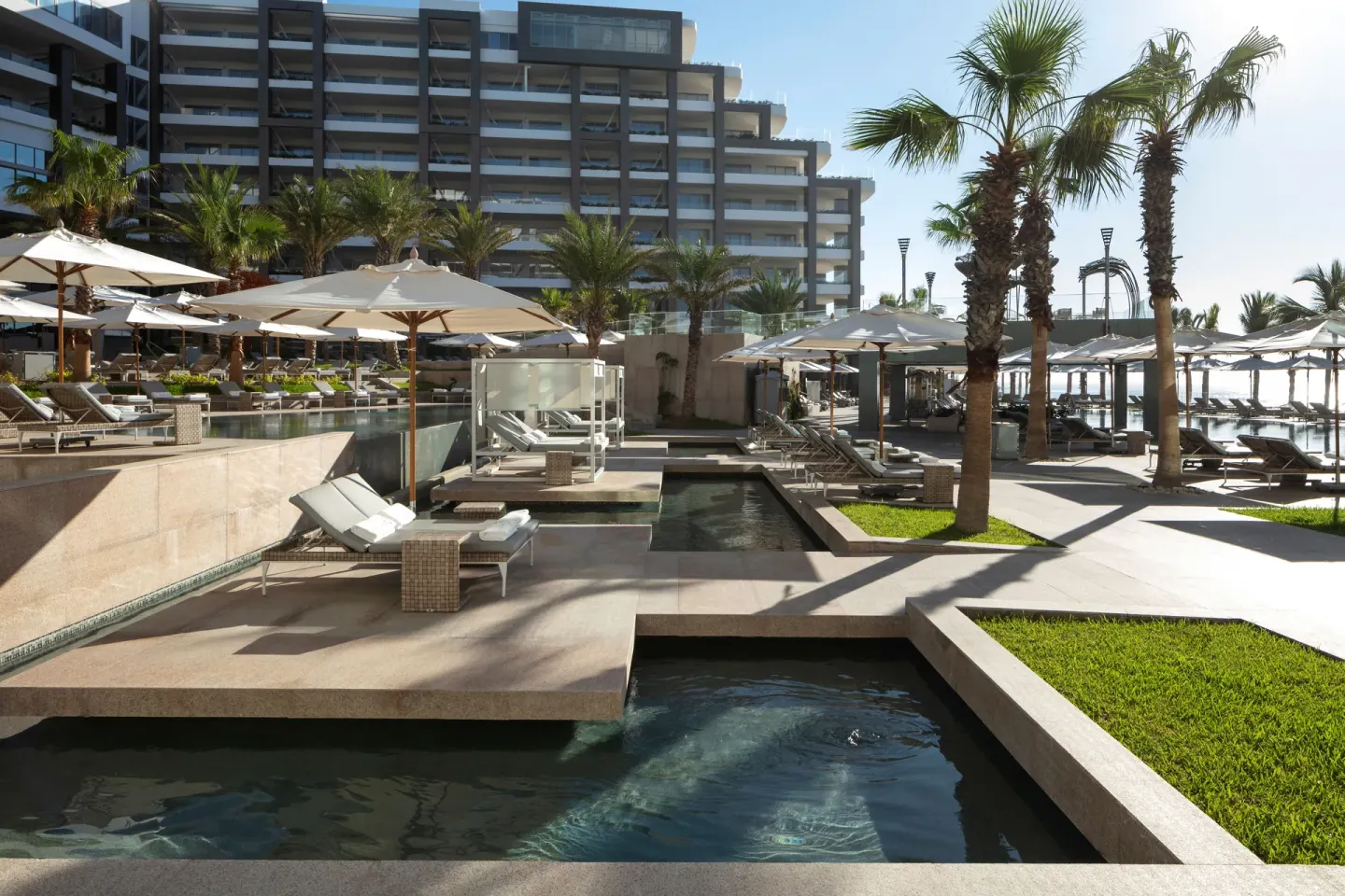 Poolside loungers, umbrellas, palms, and resort building at Garza Blanca Los Cabos.