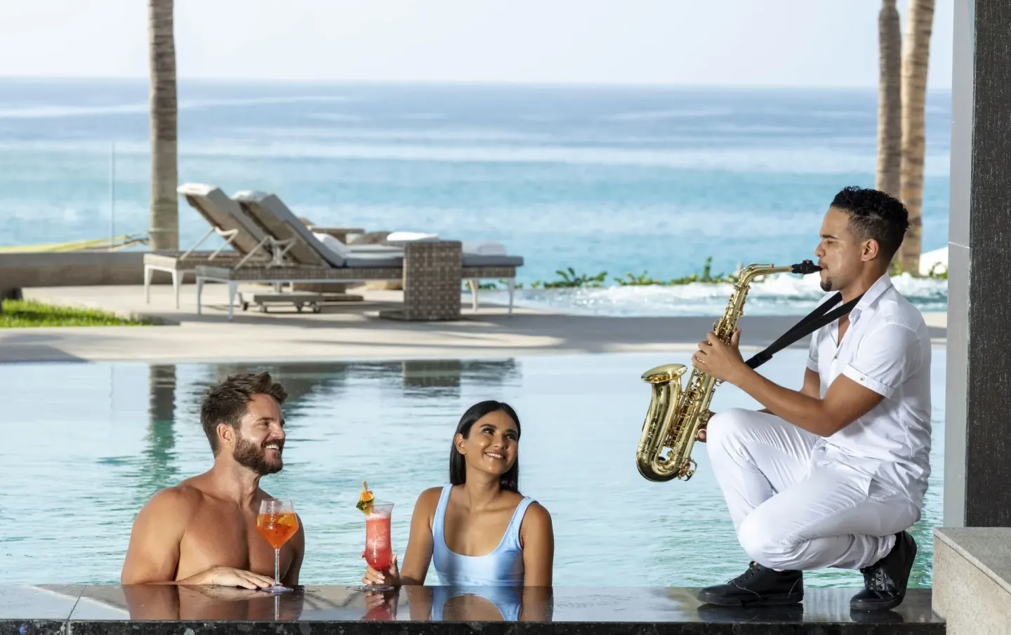 Couple with cocktails listening to a saxophonist by the pool at Garza Blanca Los Cabos.