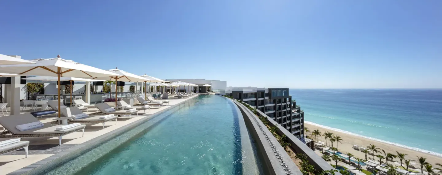 Rooftop infinity pool with loungers, umbrellas, beach, and ocean at Garza Blanca Los Cabos.