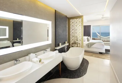 Open bathroom with soaking tub by a king bedroom at Garza Blanca Los Cabos.