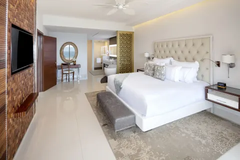 King bedroom with TV wall, bench, and ocean glimpse at Garza Blanca Los Cabos.