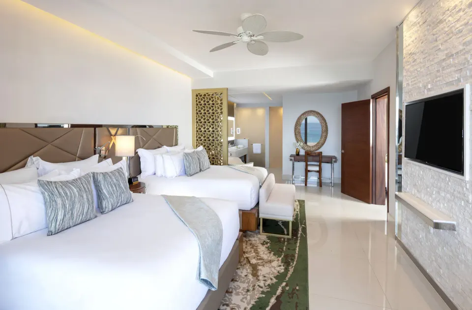 Two-bed guest room with TV wall and vanity area at Garza Blanca Los Cabos.