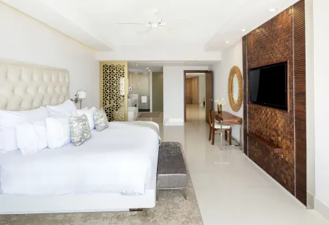 Penthouse bedroom at Garza Blanca Los Cabos with king bed, TV wall, desk, and open bathroom area.