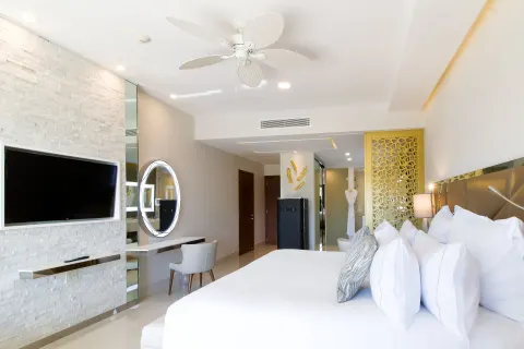 Junior Suite king bed with pillows, TV wall, mirror, and entry area at Garza Blanca Los Cabos.
