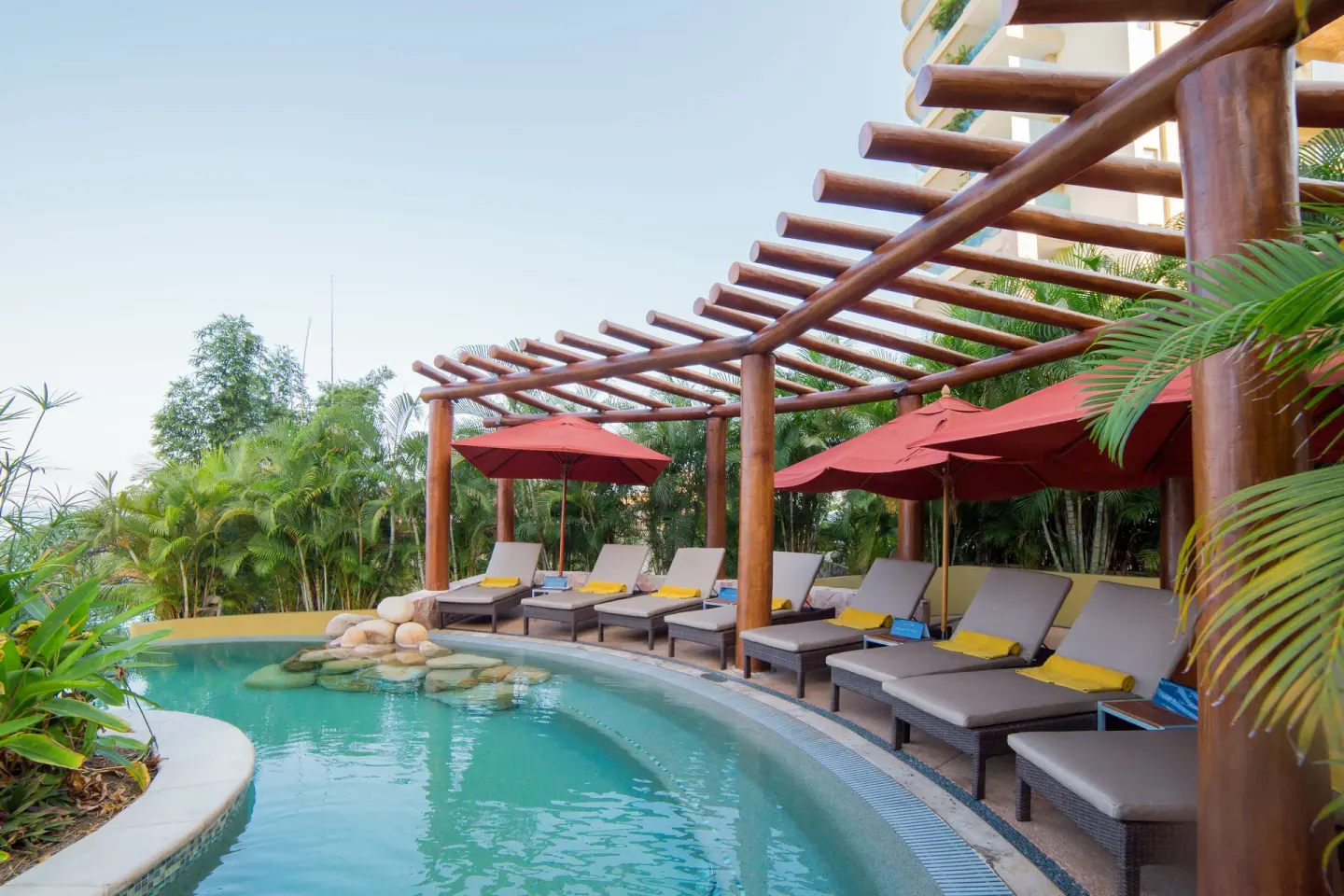 Curved pool with loungers under red umbrellas at Garza Blanca Preserve Resort & Spa.