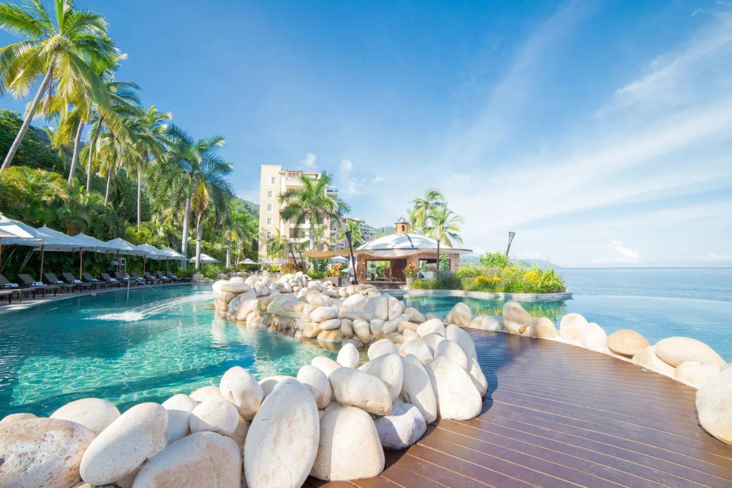 Pool, rock-lined walkway, palms, and ocean at Garza Blanca Preserve Resort & Spa.