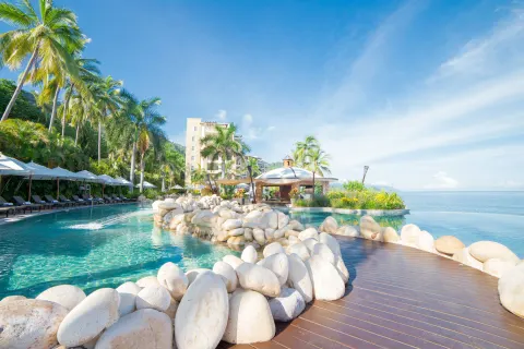 Pool, rock-lined walkway, palms, and ocean at Garza Blanca Preserve Resort & Spa.