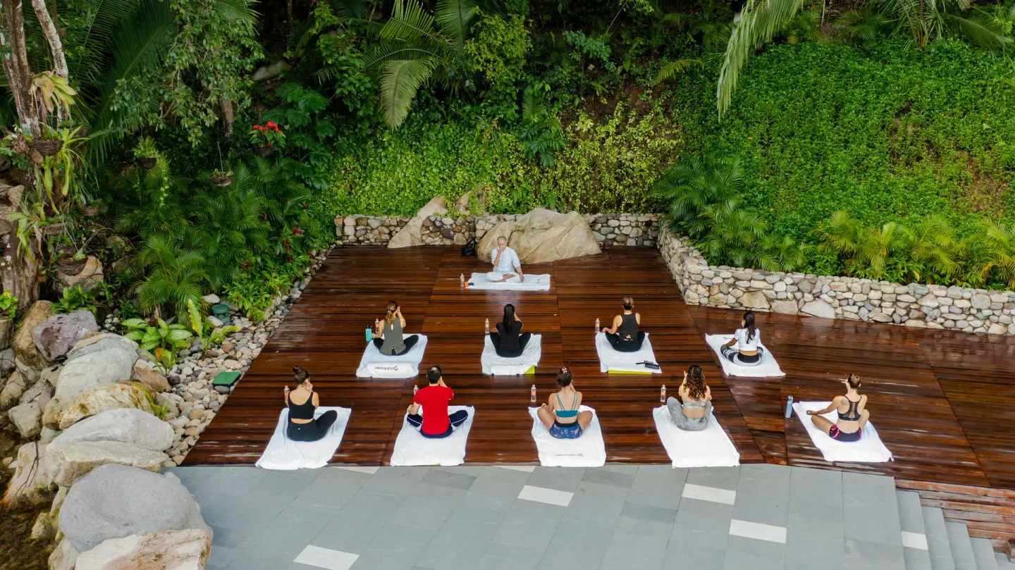 Outdoor yoga class on a wooden deck at Garza Blanca Preserve Resort & Spa surrounded by tropical greenery.