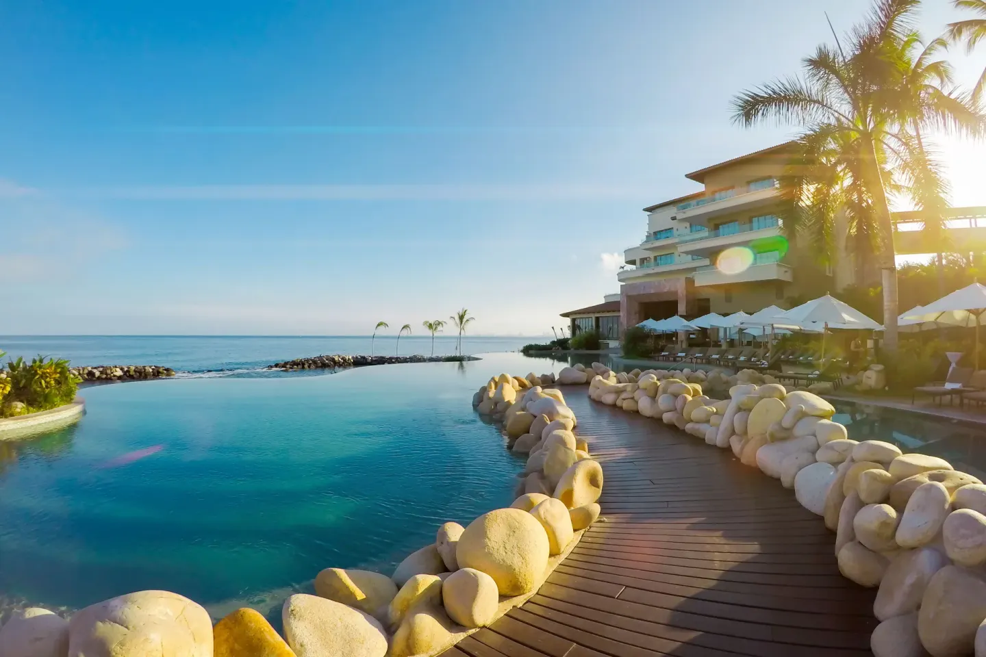 Sunlit pool walkway with ocean and umbrellas at Garza Blanca Preserve Resort & Spa.