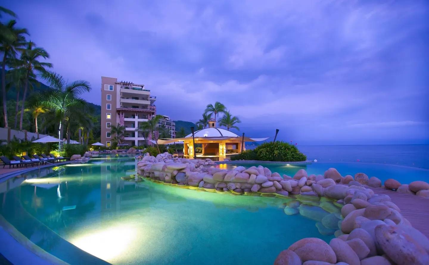 Twilight pool and oceanfront pavilion at Garza Blanca Preserve Resort & Spa under a purple sky.