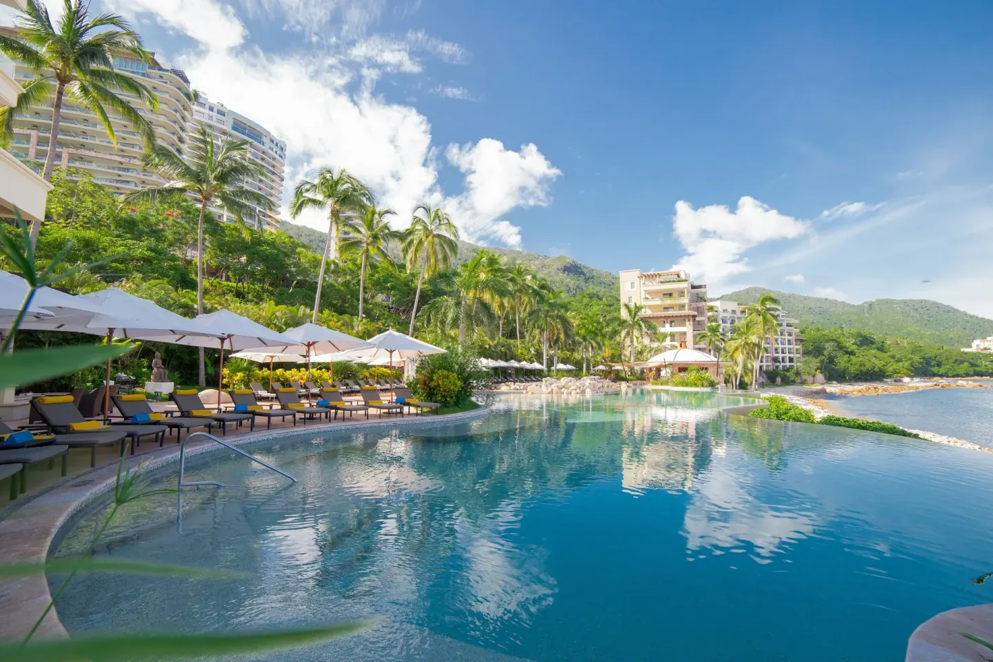 Wide resort pool with loungers, palms, ocean, and hillside at Garza Blanca Preserve Resort & Spa.