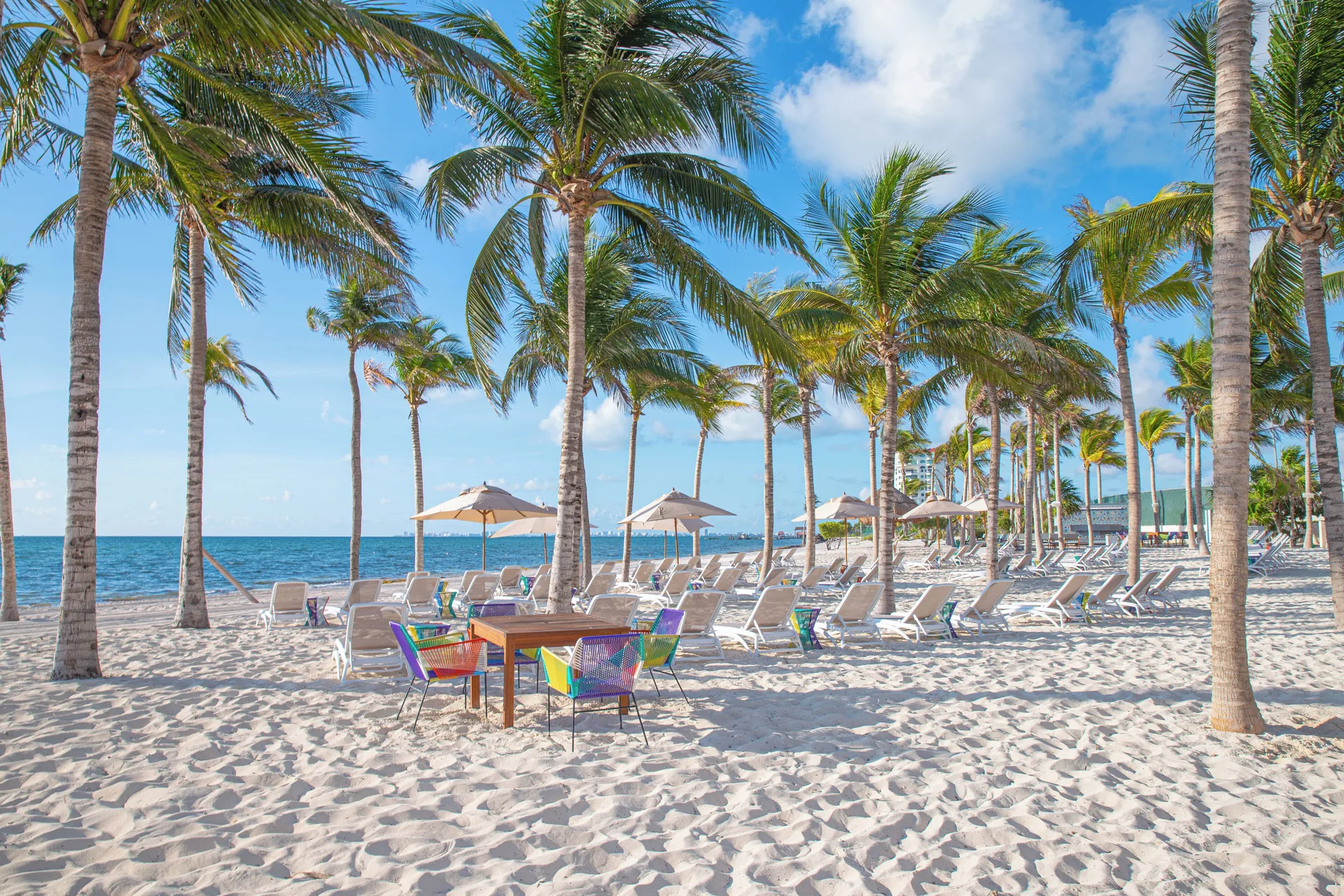 Beach loungers, umbrellas, and palm trees on the sand at Garza Blanca Resort & Spa Cancun.
