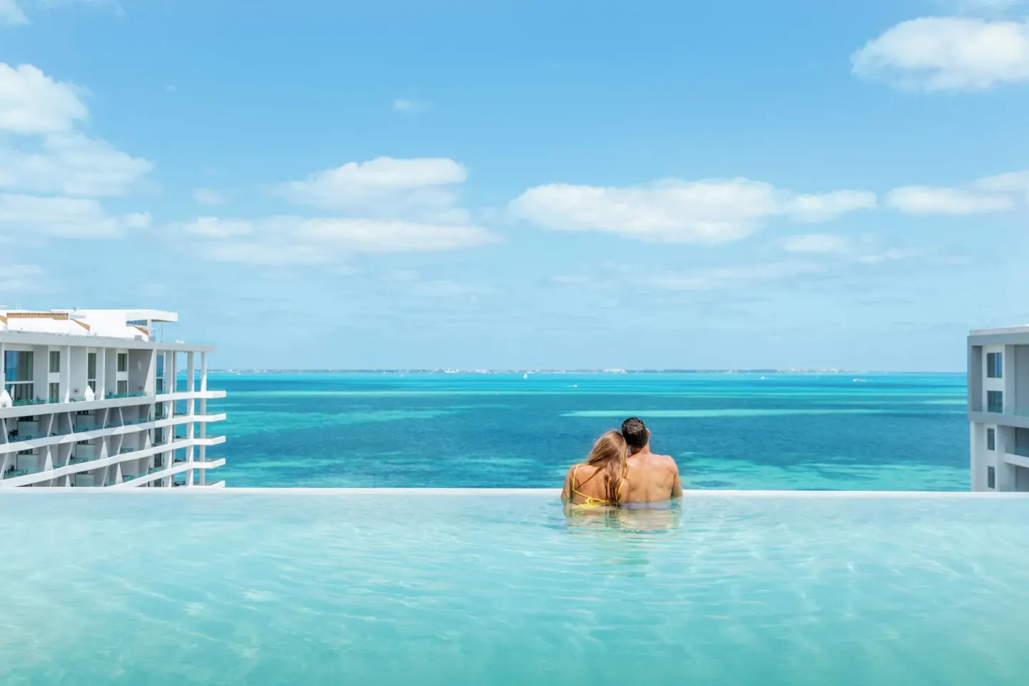 Couple sitting at the infinity pool edge at Garza Blanca Resort & Spa Cancun.