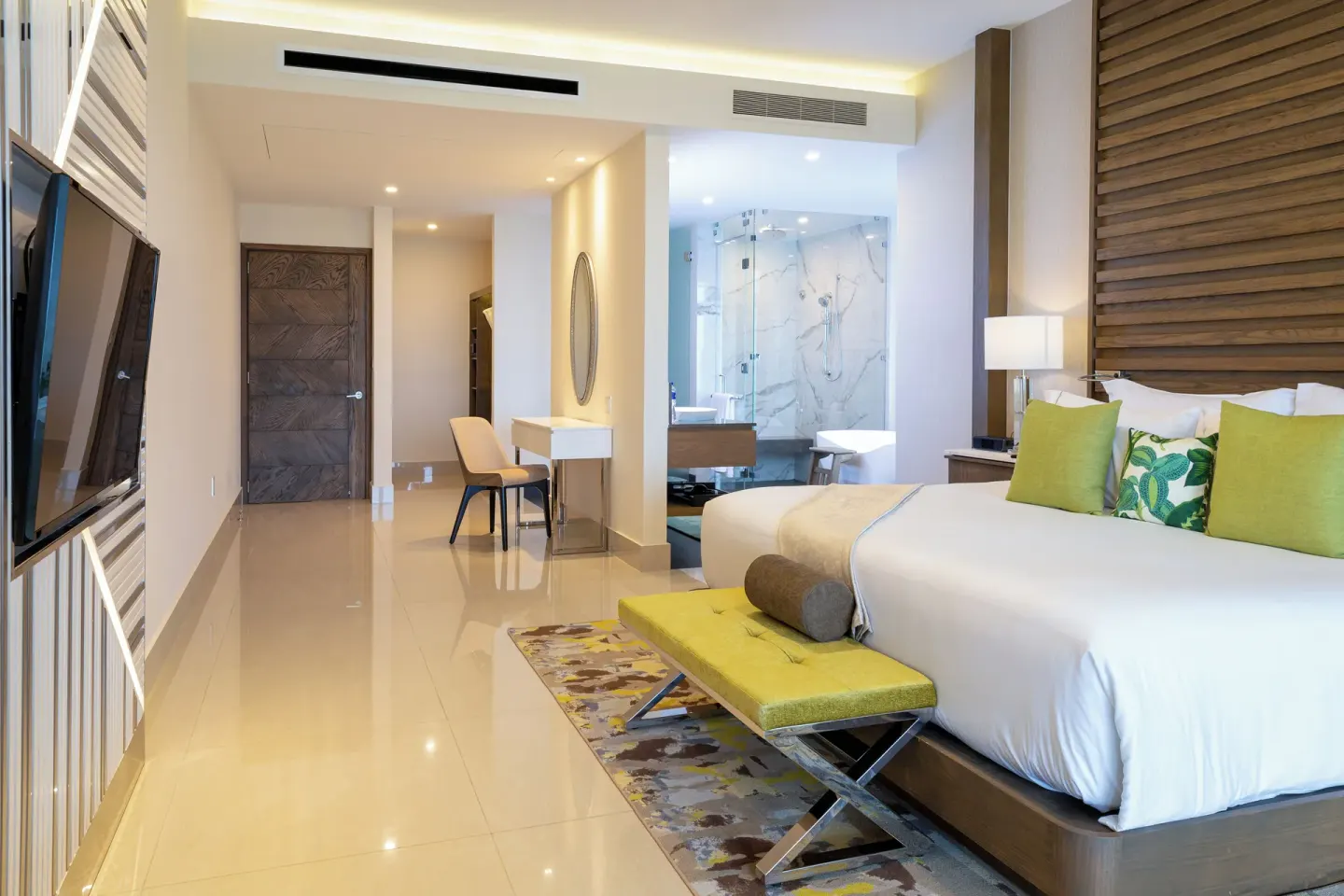 King bed guest room with TV, bench, desk and glass shower at Garza Blanca Resort & Spa Cancun.