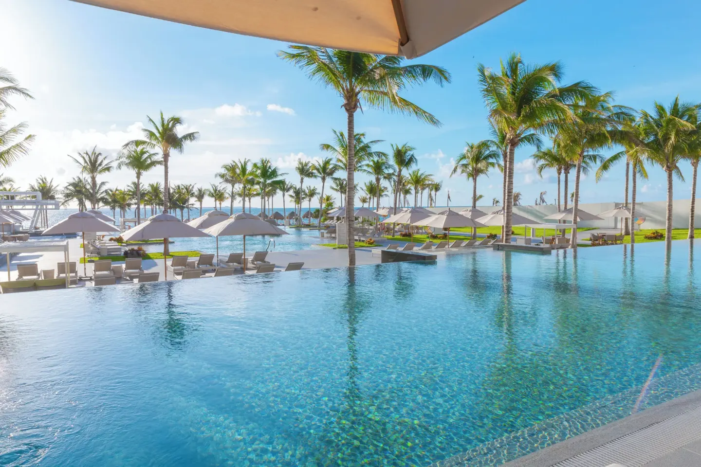 Infinity pool with palms, loungers, and umbrellas at Garza Blanca Resort & Spa Cancun.