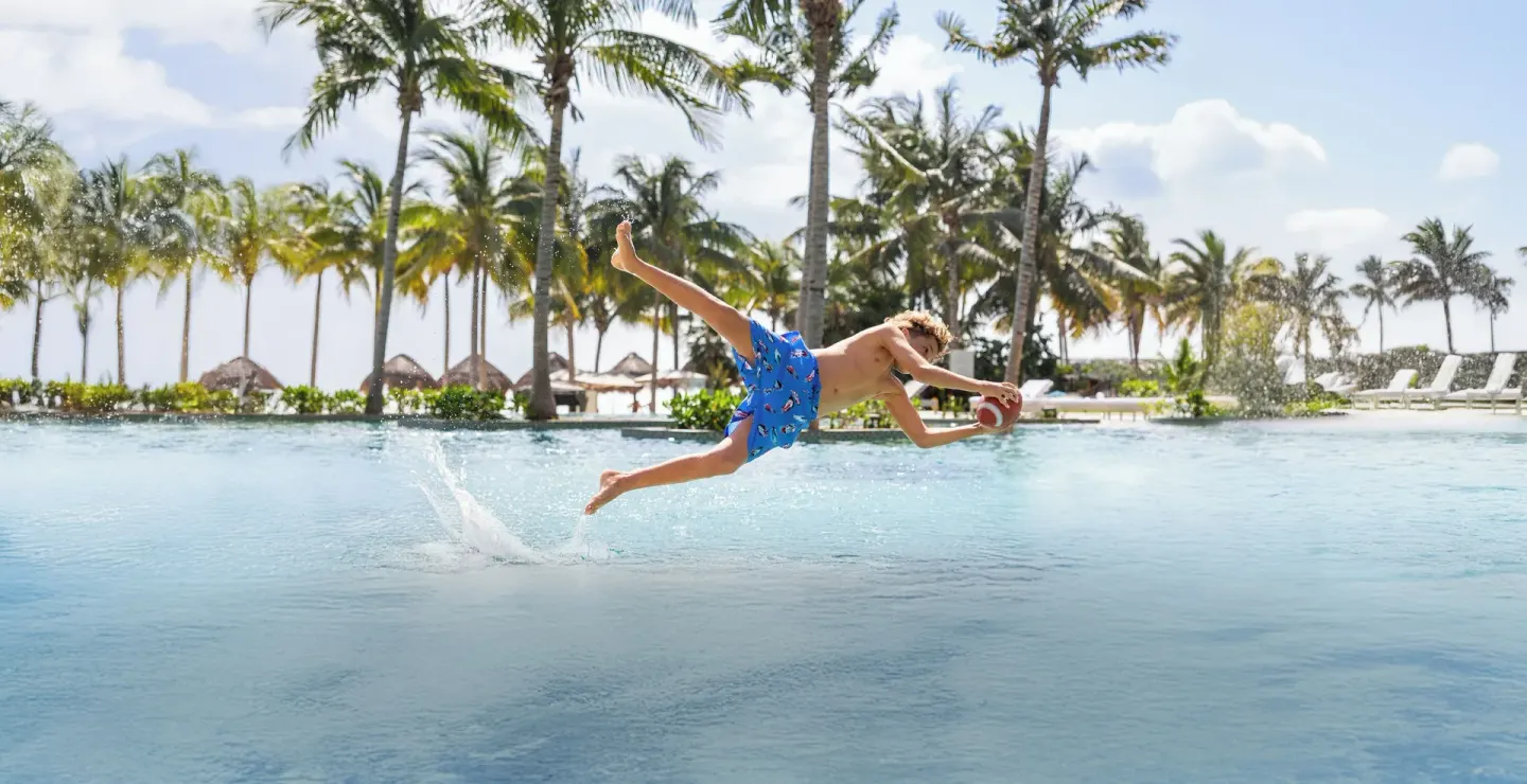 Child diving across the pool with a football at Garza Blanca Resort & Spa Cancun.