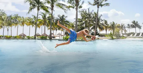 Child diving across the pool with a football at Garza Blanca Resort & Spa Cancun.