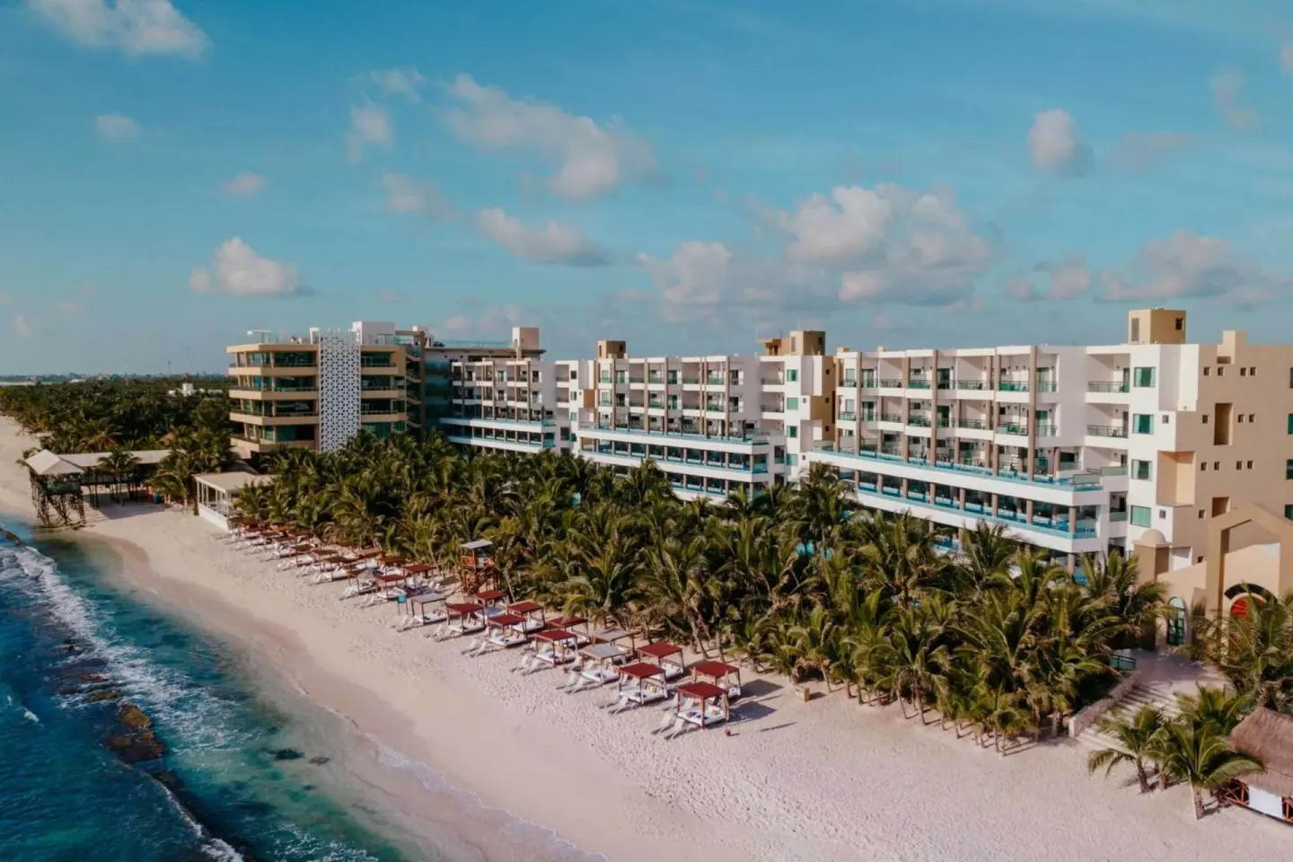 Beachfront resort buildings, palms, and cabanas at Generations Riviera Maya.