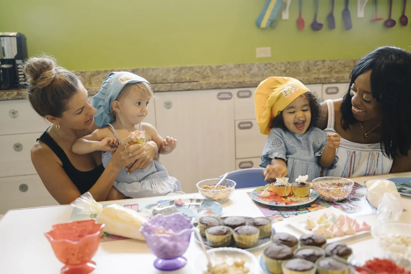 Toddlers decorate cupcakes with adults in a kitchen classroom at Generations Riviera Maya.
