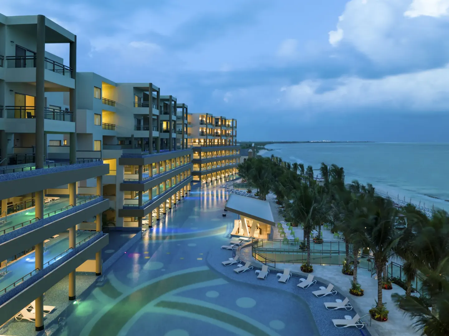 Evening view of lit resort buildings and pools by the beach at Generations Riviera Maya.