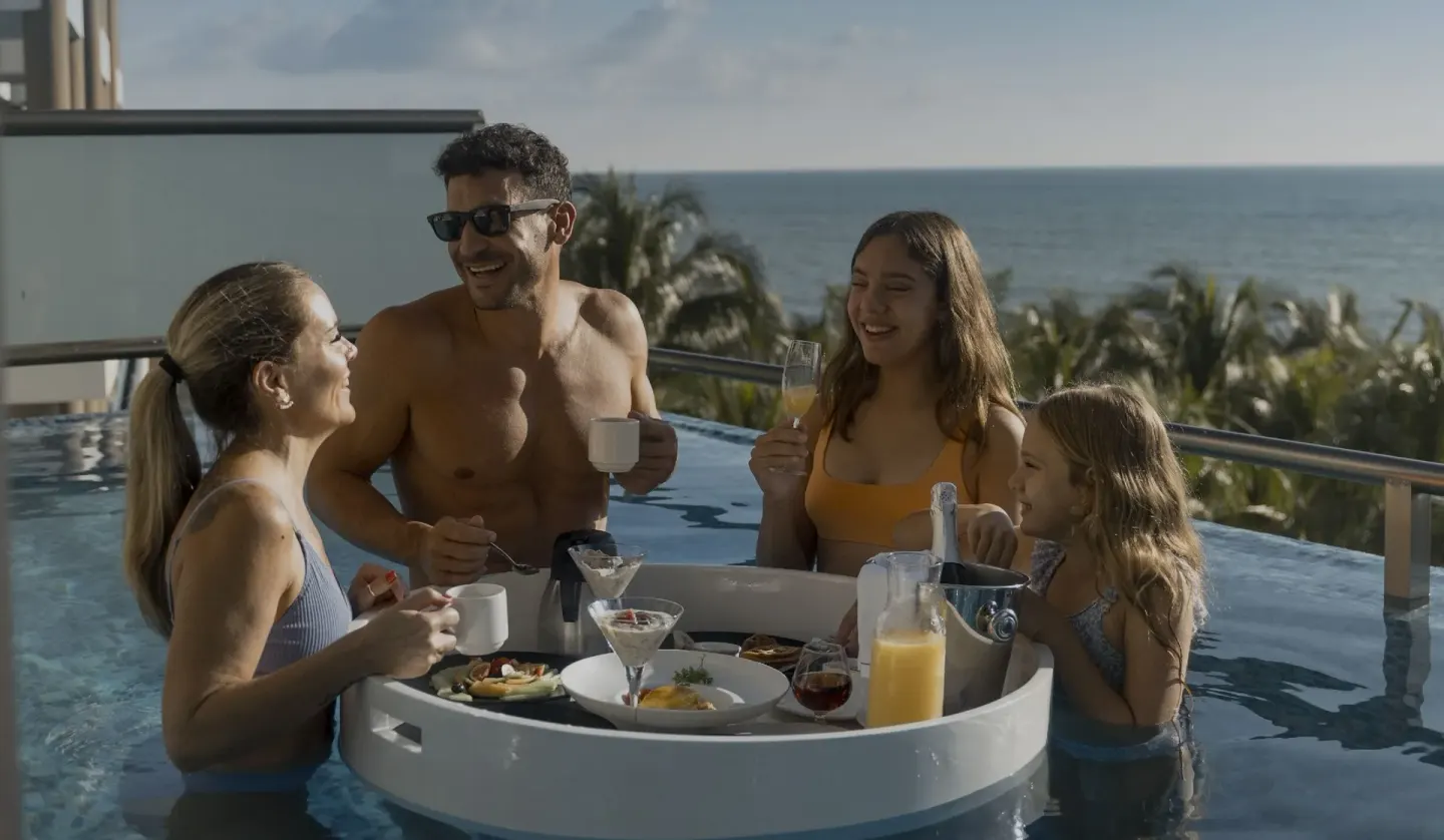 Family dining at an in-pool table with ocean behind them at Generations Riviera Maya.