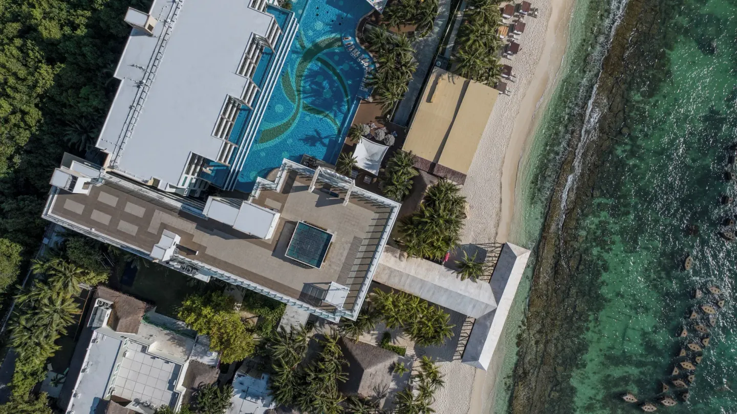 Overhead view of resort rooftops, pool, beach, and reef at Generations Riviera Maya.