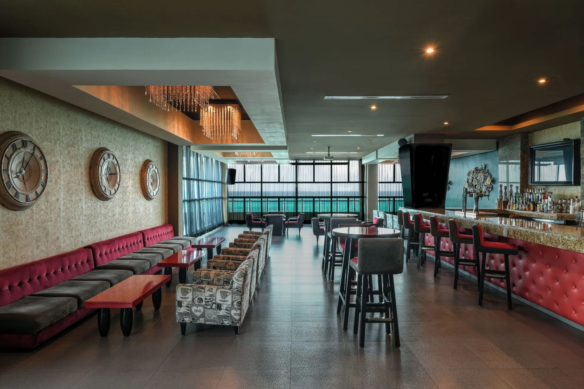 Indoor cocktail bar with red banquettes and ocean-facing windows at Generations Riviera Maya.