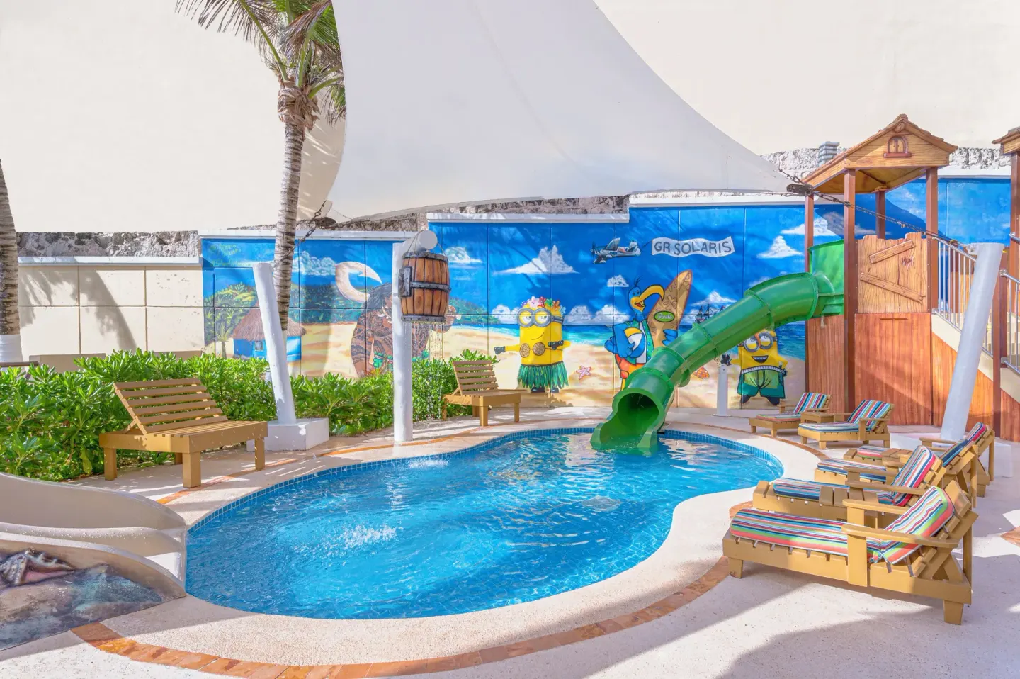 Children’s splash pool with green slide and beach mural at GR Solaris Cancun & Spa.