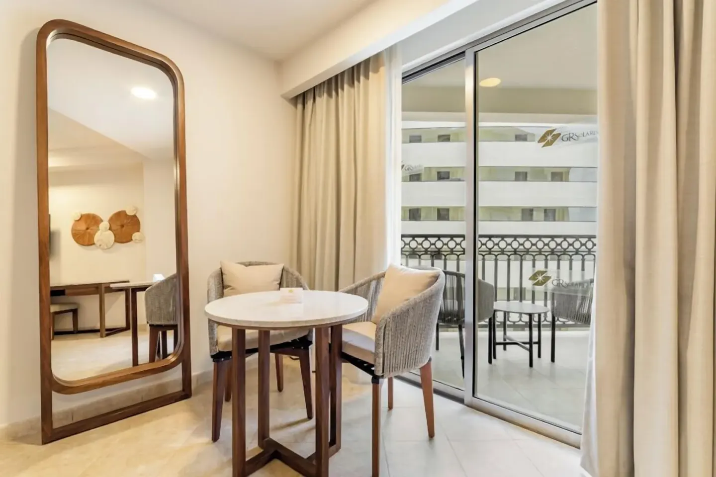 Guest room sitting area with mirror, table, and balcony doors at GR Solaris Cancun & Spa.